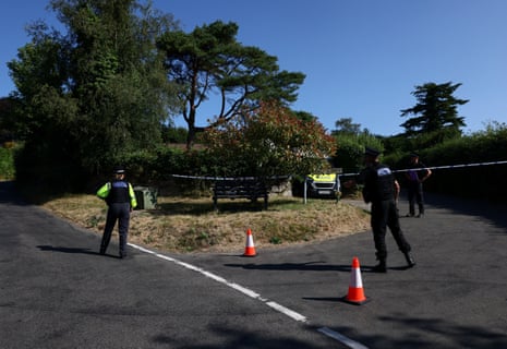 Police officers stand near a cordon tape as they investigate the home of Ann Widdecombe after she was found dead, in Haytor.
