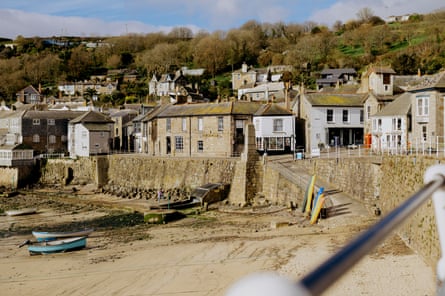 a picturesque view of Mousehole harbour in Cornwall, with some boats on the beach
