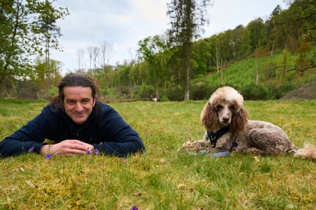 A man lying down in a meadow with a dog sitting beside him