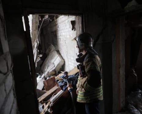 A rescue worker in protective gear and a high-visibility vest examines debris inside a damaged residential building following a drone strike on the Saltivka district in Kharkiv, Ukraine.