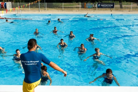 About a dozen people in the water watch Guillaume giving instruction at poolside