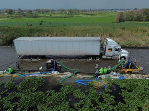 Workers use pumping equipment as a large lorry moves slowly along a flooded road in the wetlands of central Mexico