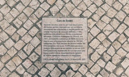 A pale-coloured plaque embedded in stonework with the title Cais do Sodré and a long paragraph of text in Portugurese beneath