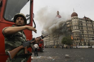 A soldier takes cover as the Taj Mahal hotel in Mumbai burns during a gunfight between the Indian military and militants inside the building on 29 November 2008