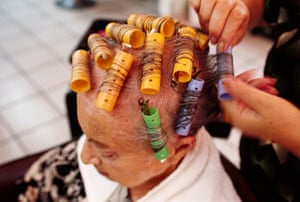 an older woman sitting having her hair put in rollers by a hairdresser