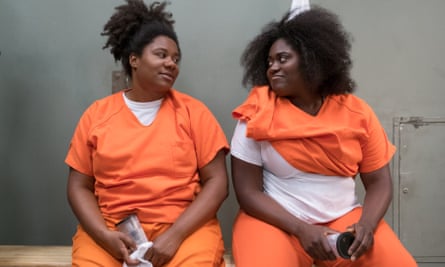 丹妮尔·布鲁克斯 (Danielle Brooks) 与艾德丽安·C·摩尔 (Adrienne C Moore) 在《女子监狱》(Orange is the New Black) 中合作； 并排坐着，两人都穿着橙色的监狱外衣和裤子，以及白色的 T 恤。