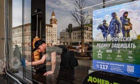 A shopkeeper wipes a window on which the advertising poster is pasted reading ‘Our profession is to defend the Motherland’ promoting the contract service in the armed forces in Moscow.