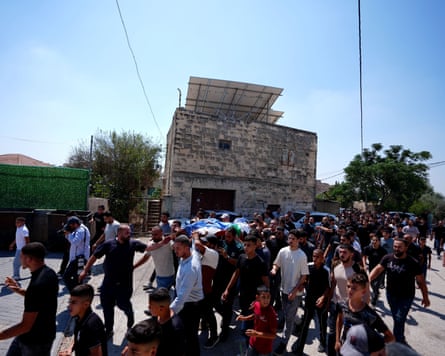 A crowd of men, some of whom are carrying a body on a stretcher that is covered with a sheet, walk along a street A crowd of men, some of whom are carrying a body on a stretcher that is covered with a sheet, walk along a street