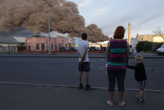 People observe a cloud of smoke from a fire in the background after a missile strike on a warehouse of an industrial and trading company in Odessa on 16 July, 2022, amid the Russian invasion of Ukraine.