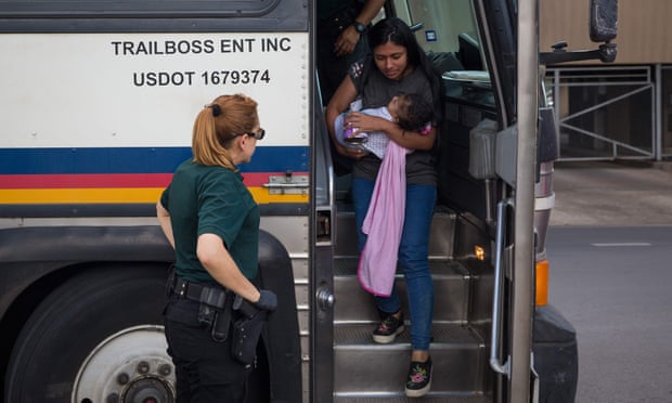 A woman carries a baby as immigrants are dropped off at a bus station shortly after being released from detention