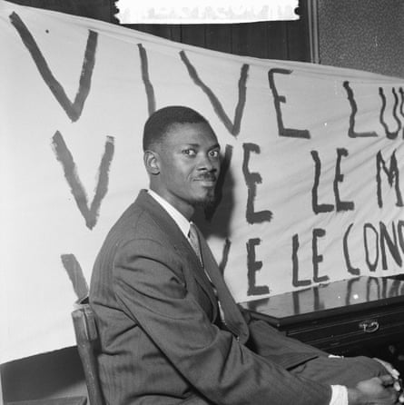 Patrice Lumumba sitting in front of a cropped banner that appears to read variants of ‘vive Lumumba’