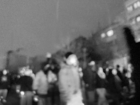 Very blurred black and white image of people in the street at night during Iran protests.