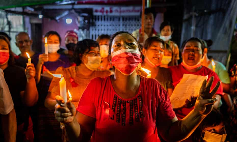 People hold candles and make three-finger salutes in a market on 5 in Yangon in protest against the military coup.