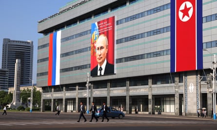 A picture of Vladimir Putin on a billboard displayed on the side of an office-type building, with Russian and North Korean flags on either side
