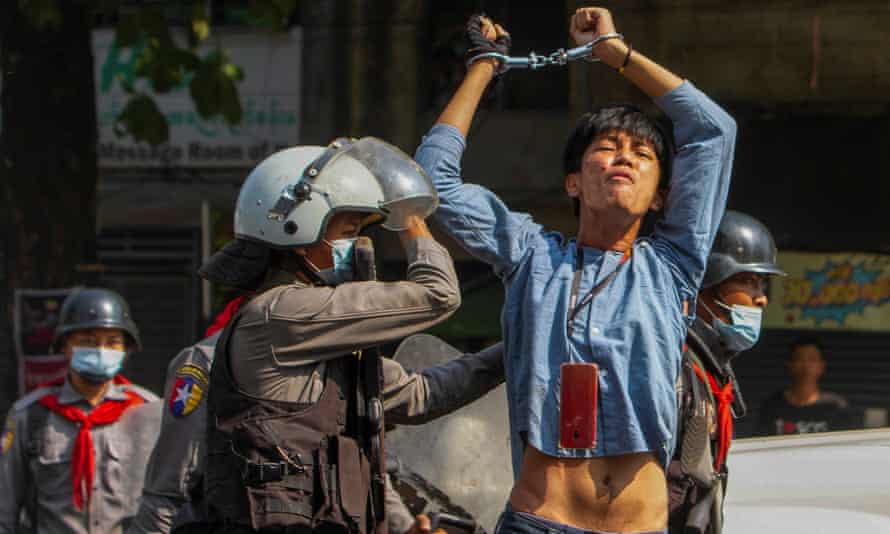 A pro-democracy protester, handcuffed and with hands above his head, is detained by riot police in Yangon.