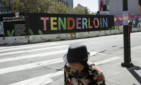 A person walks across the street from a sign for the Tenderloin neighborhood in San Francisco.