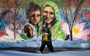A couple wearing masks walk past a mural of a mother and child in Calgary, Canada