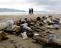 Piles of bottles and cans on beach with walkers in background