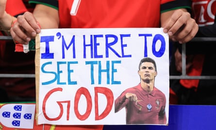 A fan holds up a sign at Portugal’s last-16 game showing a picture of Ronaldo and saying “I’m here to see the God