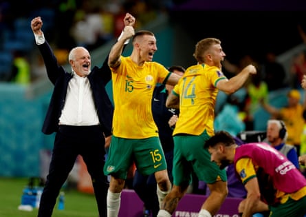 Graham Arnold celebrates with his arms in the air along with Riley McGree and Mitchell Duke