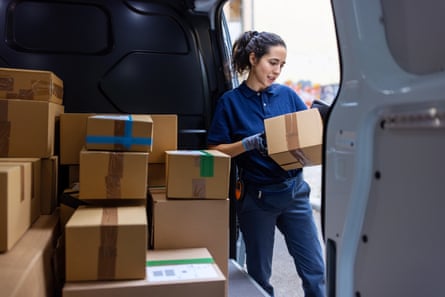 A female courier standing by a shipping van checking the parcel for delivery