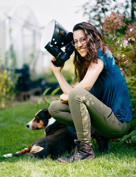 Marit van Ekelenburg crouches with her camera next to a tricolour dog, who is lying on grass