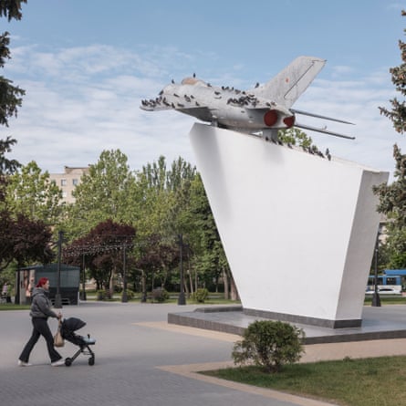 A person pushes a pram past a monument comprising a fighter jet atop a solid base