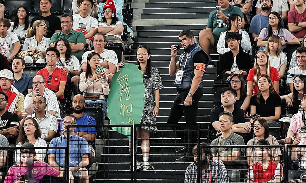 Yang holding banner next to security guard on steps between seated crowds