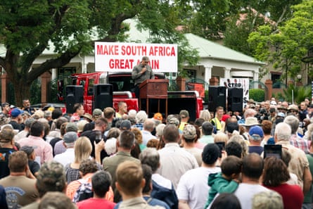 A man speaks to a crowd in front of a sign that says âÂÂmake South Africa great againâÂÂ.