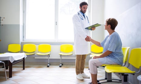 A male doctor shakes hands with a female patient in a waiting room