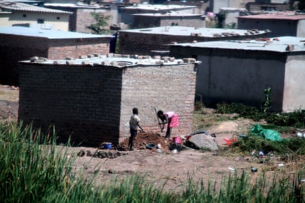 Crude windowless shacks with tin roofs weighted down with concrete blocks. Reeds are seen in the foreground