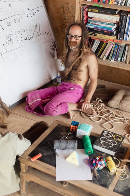 A shirtless man with dreadlocks writes on a whiteboard
