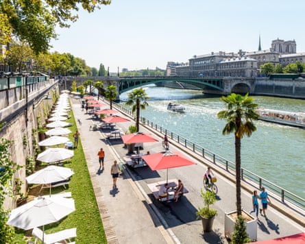 Sun umbrellas and potted palm trees line a beautifully sunny view of the Seine
