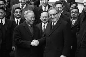 Kissinger shaking hands with an older Asian man while westerners and Vietnamese men look on