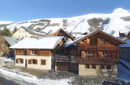 A wooden chalet with snow-covered roof stands before snowy mountains in Les Deux Alpes