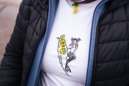 A closeup of Gabriella’s mimosa-shaped brooch pinned to her T-shirt with an illustration of a mermaid with a surfboard