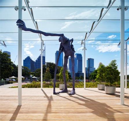 Large metal sculpture of a monster standing on a wooden deck overlooking green space in an urban setting