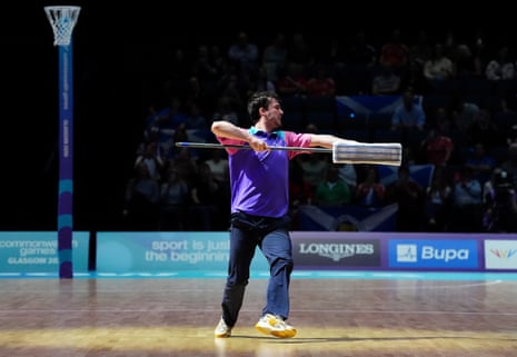 A man dances with a mop on the netball court.