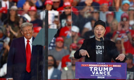 Elon Musk and Donald Trump stand behind bulletproof glass at one of Trump's campaign rallies