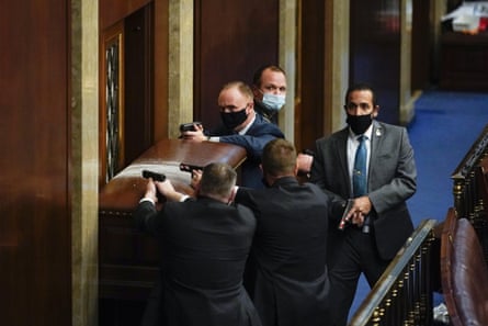 Police with guns drawn stand near a barricaded door in the House chamber.