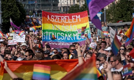 Protesters march in Budapest, holding up banners in the LGBTQ+ Pride flag colours 