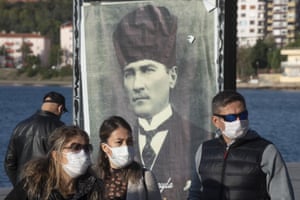 Turks wearing masks as they walk past a poster of the republic’s founder, Mustafa Kemal Ataturk, in Canakkale.
