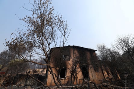 A house burned by a wildfire, with blackened trees around it.