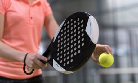 A woman holds a padel racket and a ball