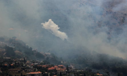 Smoke rising from hilly forest with houses in nearby.