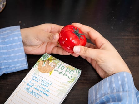 A woman holds a pomodoro timer next to a ‘to-do’ list of tasks.