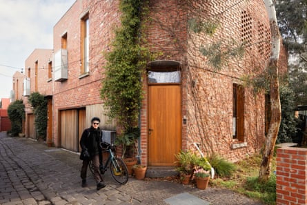 A man walks along a street wheeling a bike in front of brick townhouses