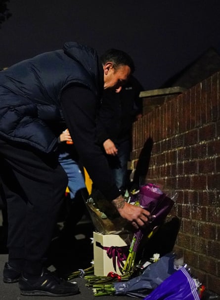 A man in a padded jacket placing flowers near where a man was stabbed to death in Uxbridge, London