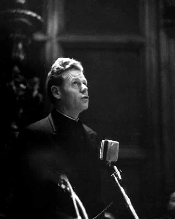 Photo of Kung lit from above by a church pillar, looking into the light, with two microphones in the foreground