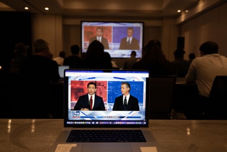 laptop screen showing two men wearing suits side-by-side as a projector plays the same image on the wall behind it